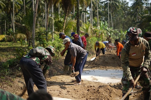 Warga dan Anggota TNI saling bergotong - royong memperbaiki jalan di Banjar Pebuhana dalam progran TMMD